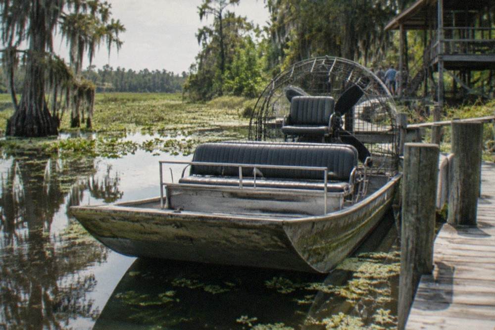 A flat-bottomed airboat parked at a wooden dock in a cypress swamp