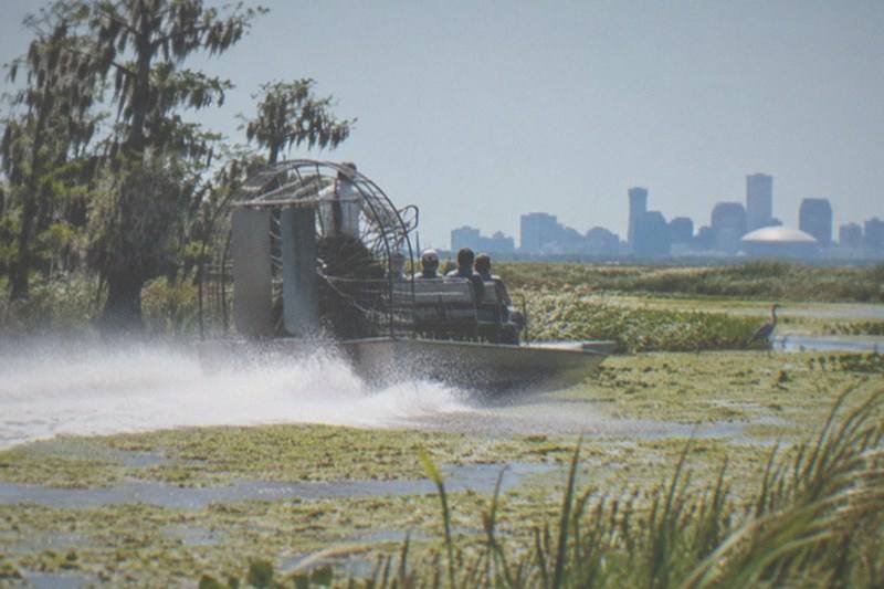 Airboat speeding across open Louisiana swamp water, propeller cage overhead