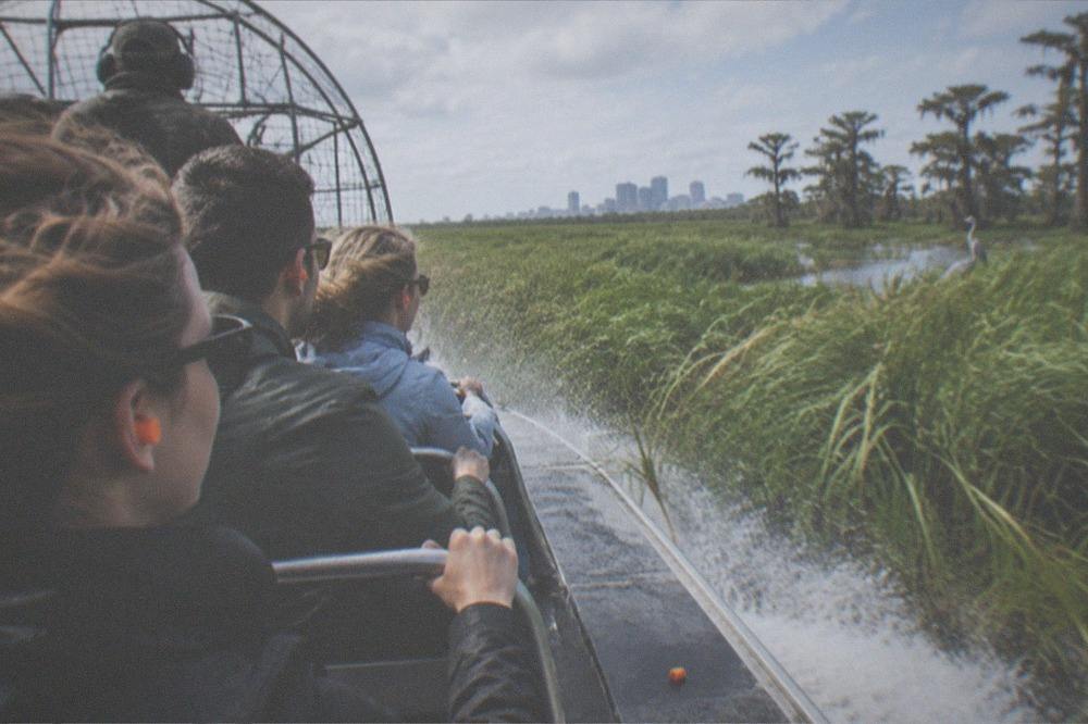 Passengers in ear protection on an airboat moving fast through tall swamp grass