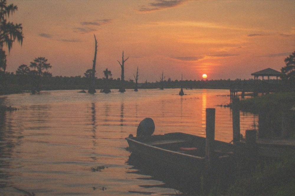 A wide bayou channel at dusk with grassy banks and scattered cypress snags