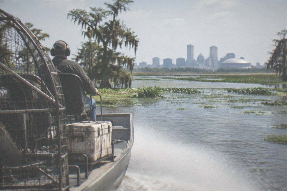 An airboat with a large propeller at the rear speeding along open swamp water