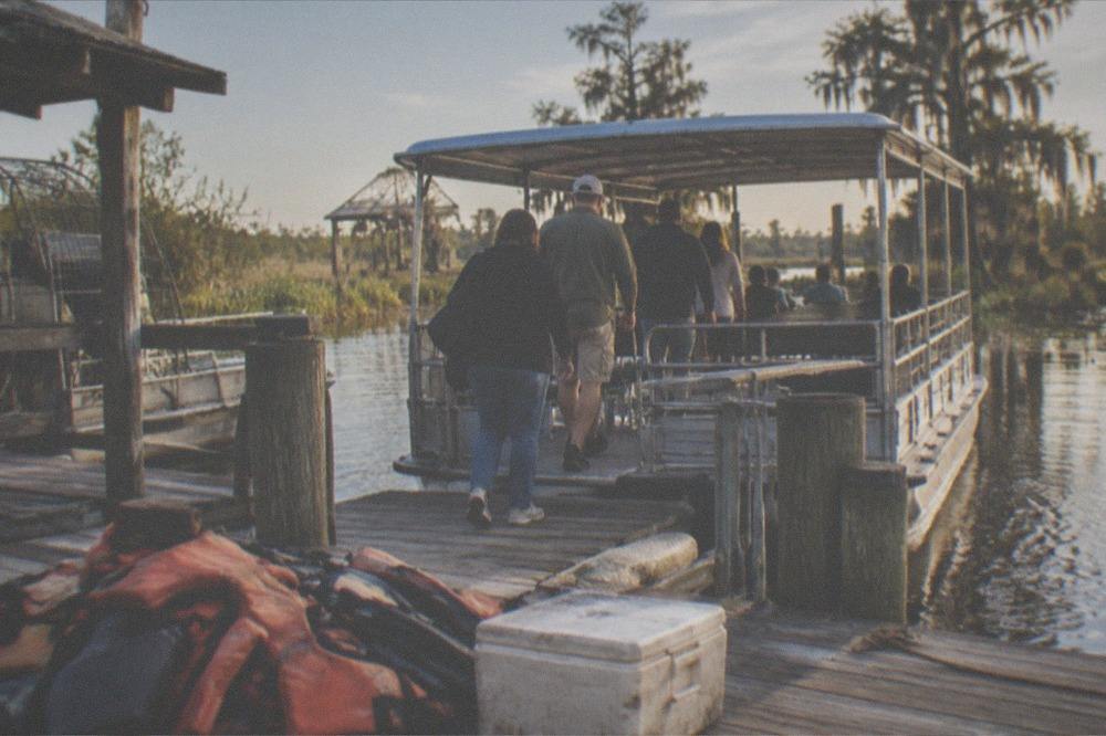 A busy swamp tour dock with passengers boarding a covered pontoon boat in warm afternoon light