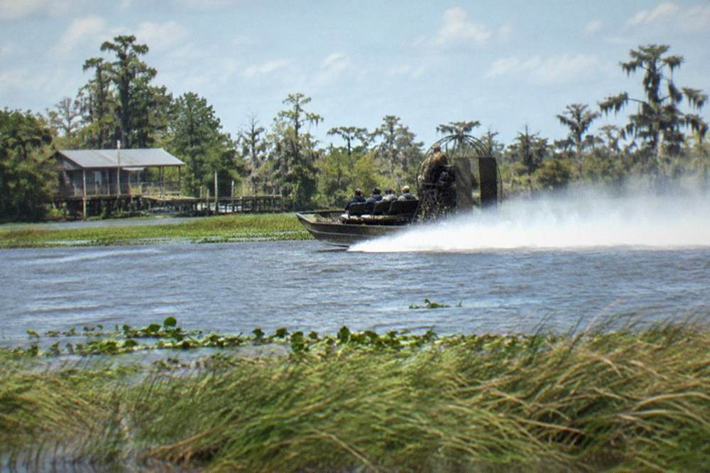 An open airboat with a large fan engine cruising fast through open swamp water
