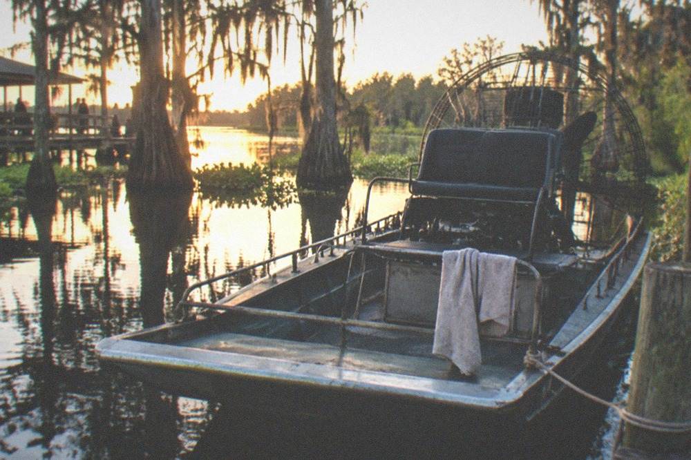 An airboat parked at a wooden dock with cypress trees reflected in still water