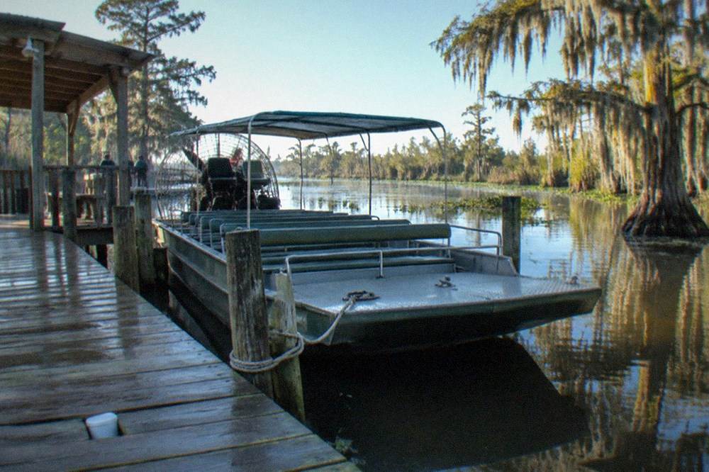 A small tour boat tied at a wooden dock beside a swamp launch area