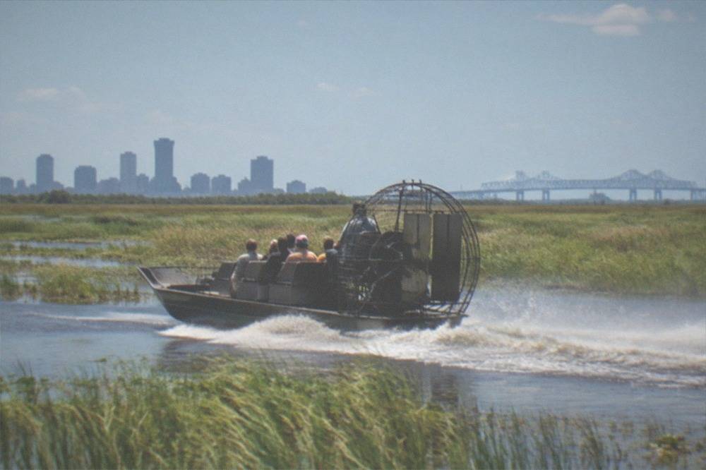 Small airboat with passengers moving fast across open swamp water