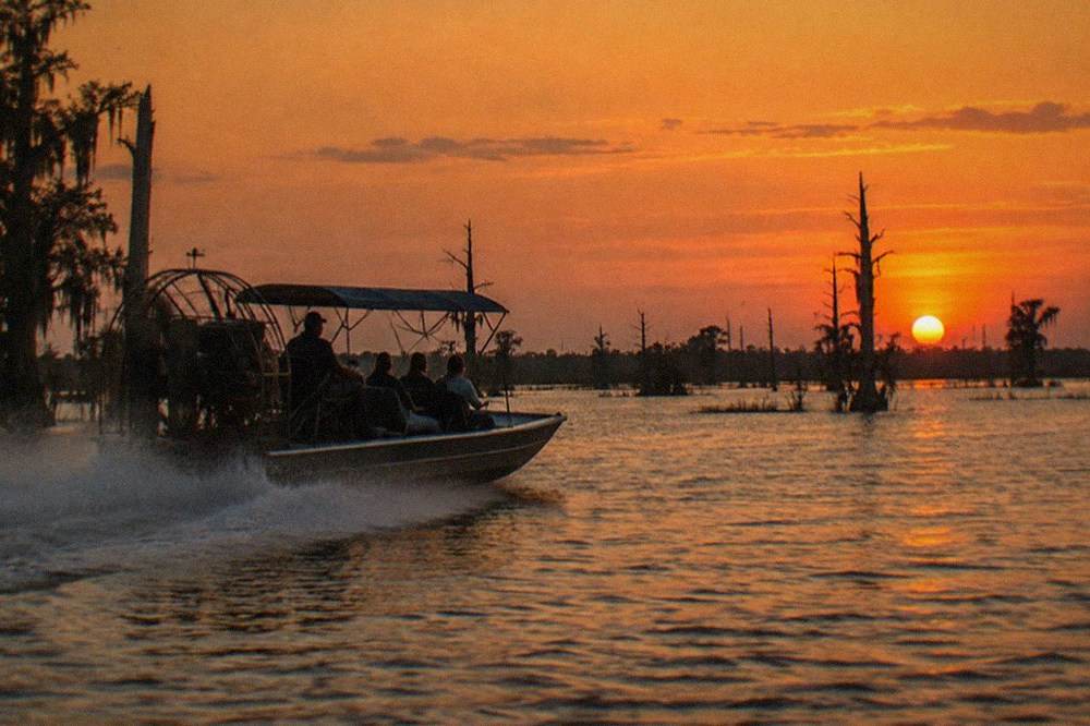 Small airboat with canopy frame speeding across open swamp water at dusk