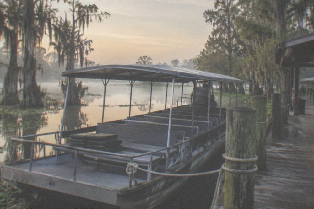Empty covered tour boat moored at a wooden swamp dock before departure