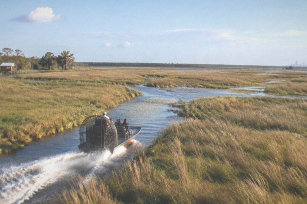 Small airboat speeding through open marsh grass under a wide sky