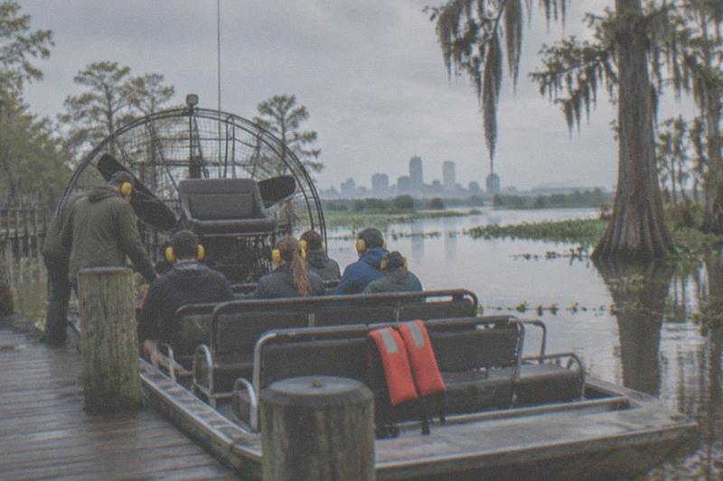 Small-group airboat waiting at a swamp dock with riders wearing ear protection before departure