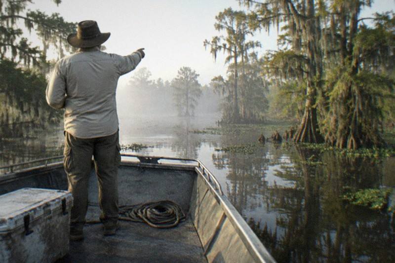 Swamp tour guide at the bow of a Honey Island boat gesturing at the treeline