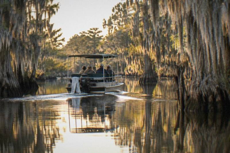 Boat touring a Honey Island waterway with moss-draped cypress swamp on each side