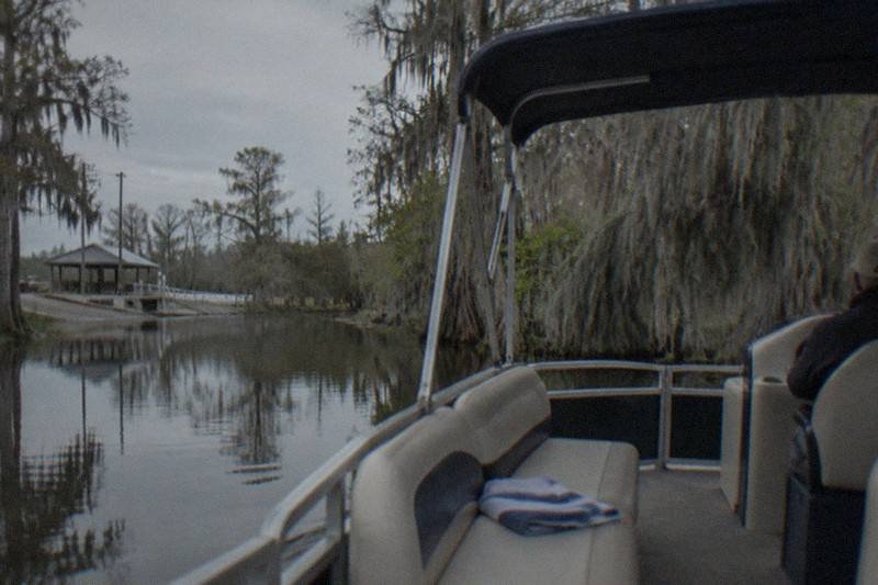 Covered pontoon boat moving through a Manchac bayou past cypress draped in Spanish moss