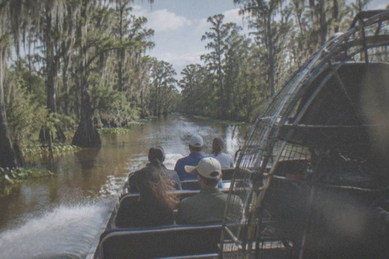 Six-passenger airboat skimming a narrow Louisiana swamp channel, propeller fan behind